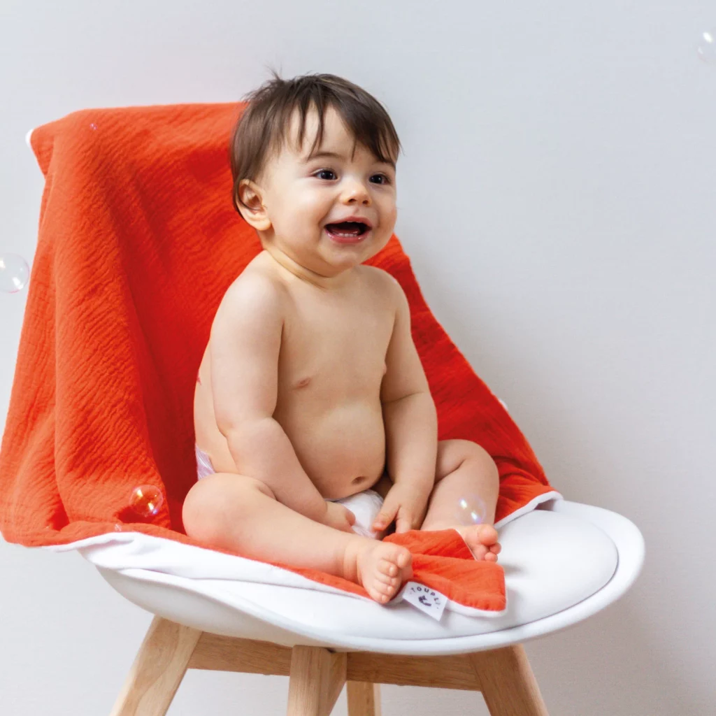 Bébé souriant assis sur une chaise avec un plaid Toupli orange